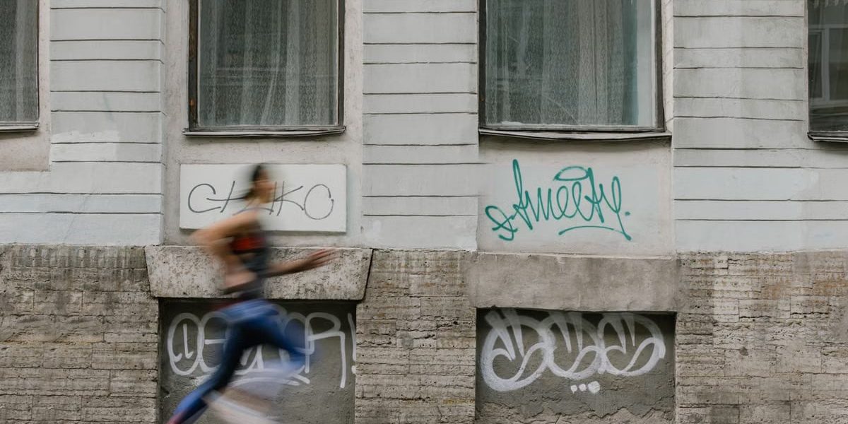 Blurred motion of a woman running past a graffiti-covered urban wall. Captures dynamic energy.