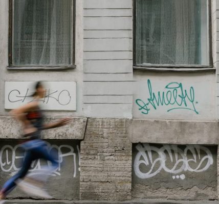 Blurred motion of a woman running past a graffiti-covered urban wall. Captures dynamic energy.