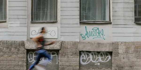 Blurred motion of a woman running past a graffiti-covered urban wall. Captures dynamic energy.